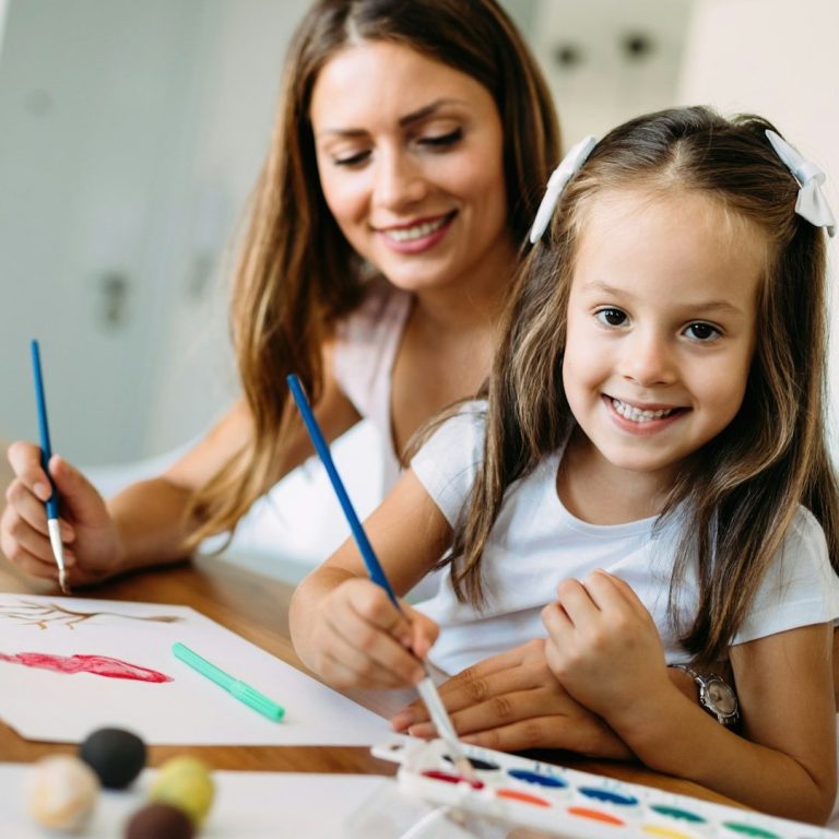 Educated Governesses | London & Overseas Woman and girl painting together, smiling, with art supplies on a table. Educated Governesses.