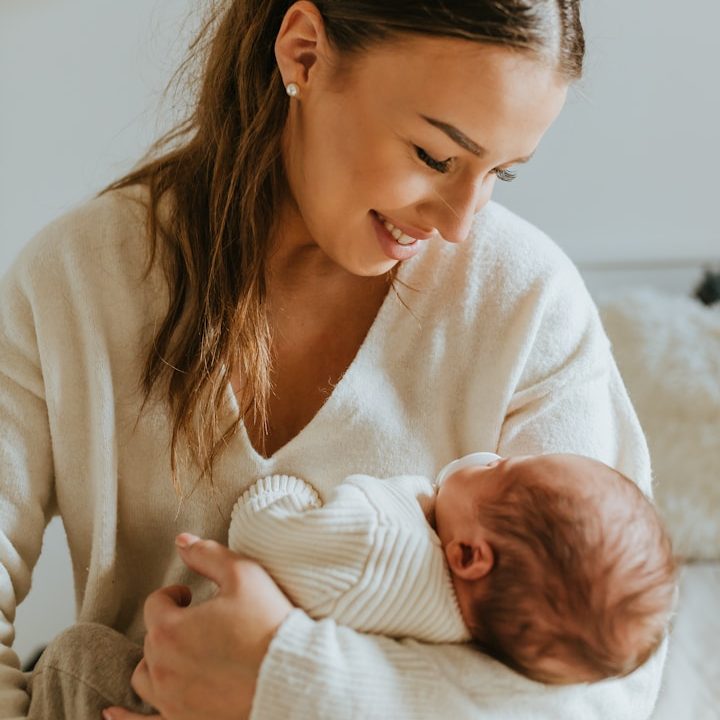 Dedicated Nannies for Families | London, UK & Overseas Smiling woman in a light sweater cradles a newborn baby in her arms. Nanny.