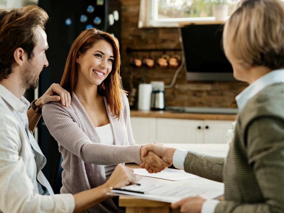 Nanny & Private Household Staffing Services for Families | UK & Overseas A woman shakes hands with a couple in a modern kitchen setting. Nanny Consulting Services for Families in London, UK and Overseas.