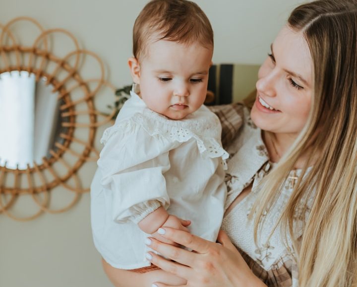 Governess | Nanny | Tutor | Bel-Rose Int. A mother holds her baby in a bright room, smiling at each other. Childcare and Education: UK Nanny Agency.